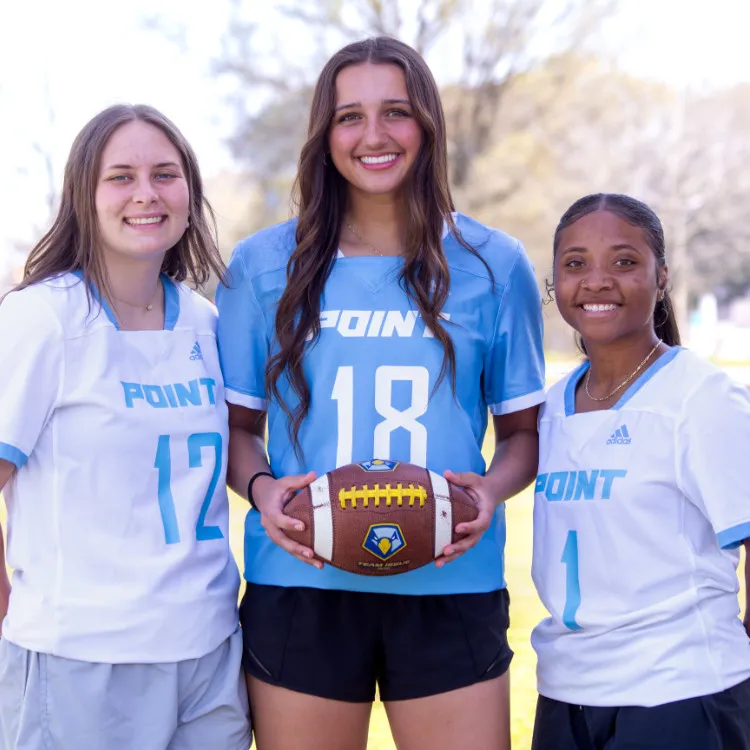 Three women in a flag football jersey holding a football